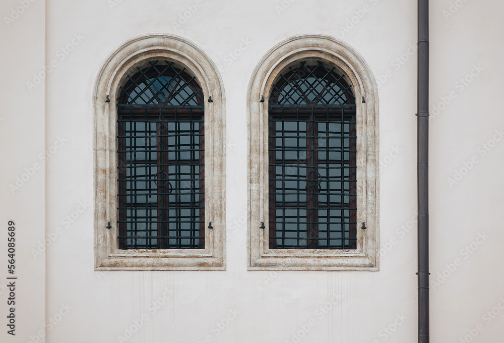 Two antique old windows with black iron bars framed on a light grey wall. The Jesuit Church in Lviv.