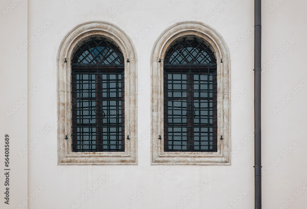 Two antique old windows with black iron bars framed on a light grey wall. The Jesuit Church in Lviv. Two antique old windows with black iron bars framed on a light grey wall. The Jesuit Church in Lviv.