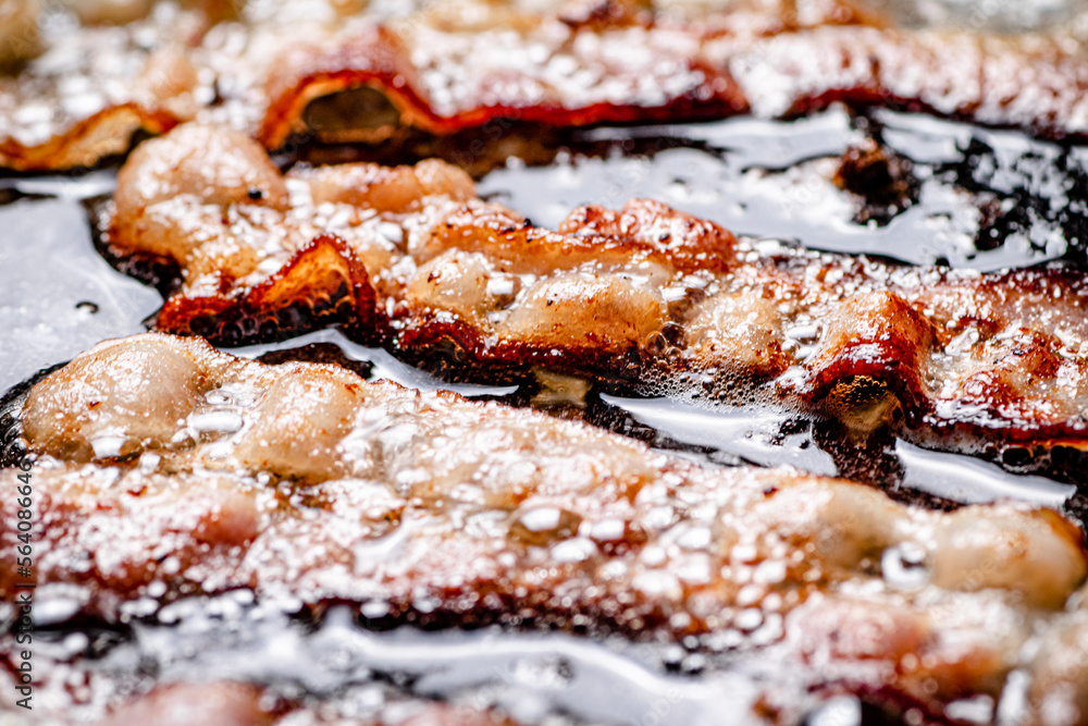 Pieces of bacon are fried in boiling oil with air bubbles. 