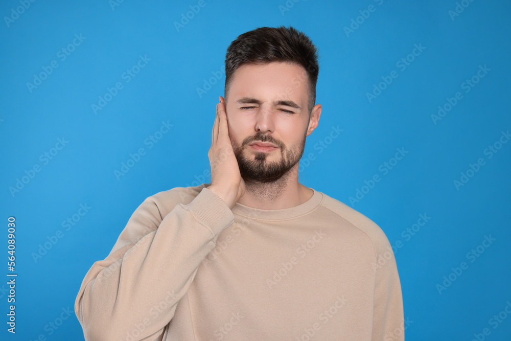 Young man suffering from ear pain on light blue background Young man suffering from ear pain on light blue background
