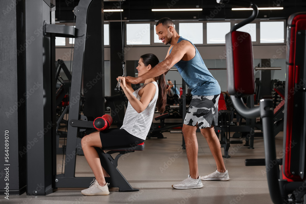 Happy trainer showing woman how to do exercise properly in modern gym Happy trainer showing woman how to do exercise properly in modern gym