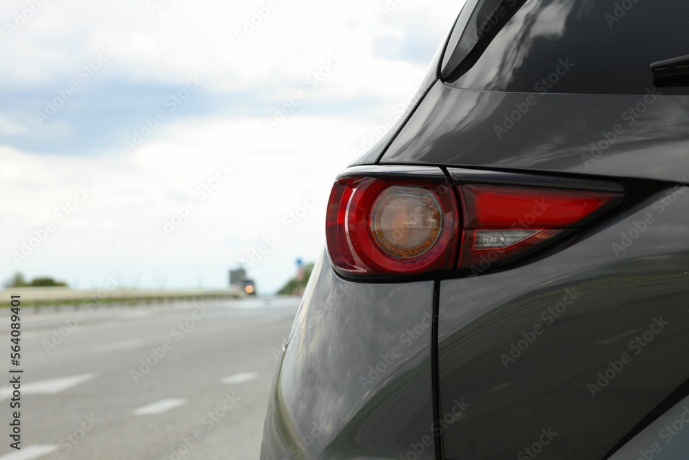 New black modern car on asphalt road, closeup of taillight. Space for text