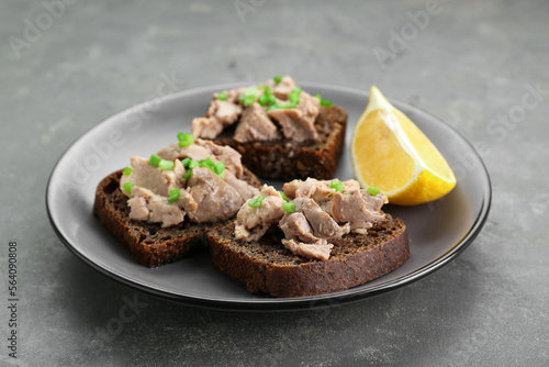 Tasty sandwiches with cod liver, lemon and green onion on light grey table