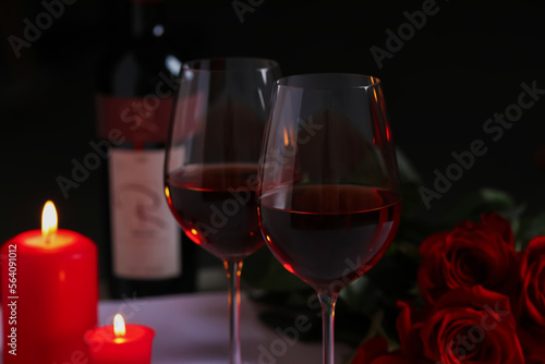 Romantic table setting with glasses of red wine, rose flowers and burning candles