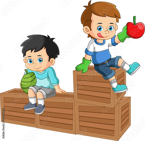 Two boys sitting on top of a fruit crate holding fresh watermelon and apple fruits