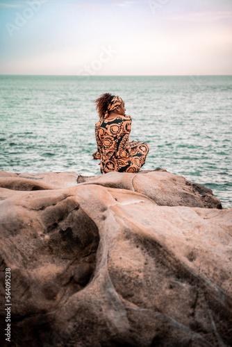 African model looking at the camera dressed in kaftan, sit in the rock 