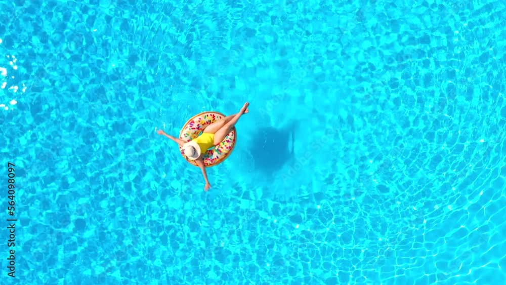 Top down view of a woman in yellow swimsuit lying on a donut in the pool