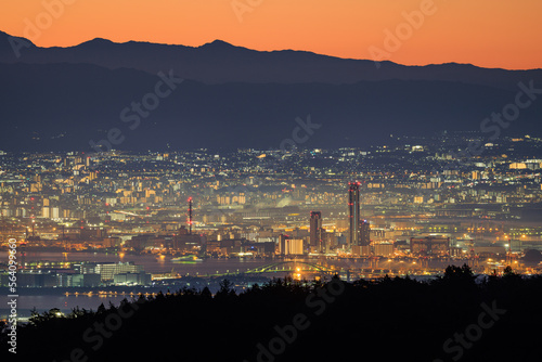 Lights from city mix with orange dawn glow over distant mountains