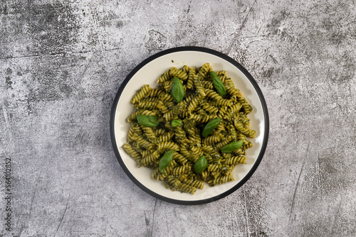 Fusilli pasta with Spicy Pesto and fresh basil leaves on a round plate on a dark gray background. Top view, flat lay