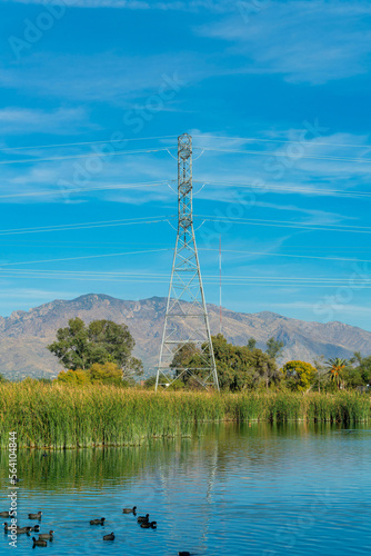 Power or telephone tower used to hang lines with metal exteror in background and tranquil lake with foliage