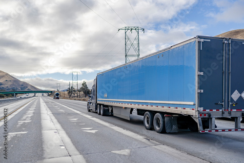 Big rig gray semi truck transporting cargo in dry van semi trailer driving on the straight wide highway road