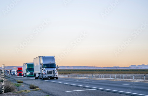 Professional long haul big rigs semi truck transporting cargo in semi trailers running on the straight highway road at twilight