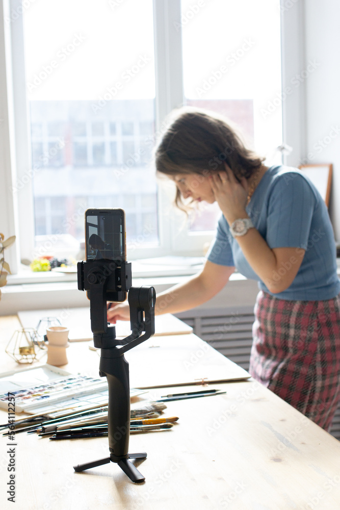 Young woman painting a picture with watercolor and filming video at wooden table Young woman painting a picture with watercolor and filming video at wooden table