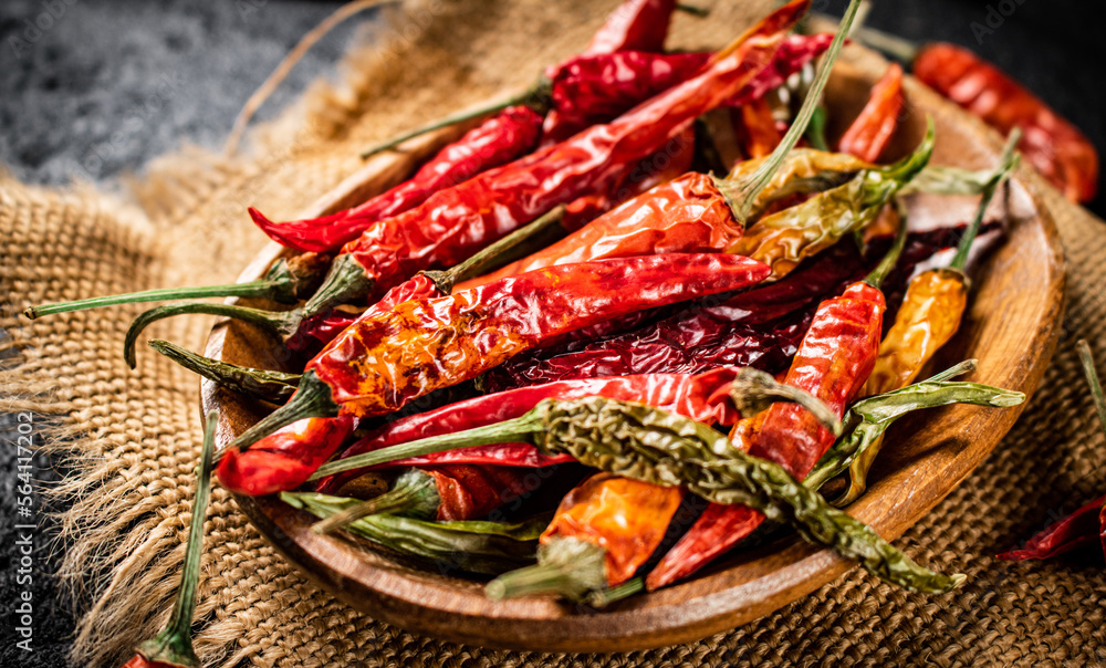 Pods of dried chili peppers in a wooden plate on a napkin. Pods of dried chili peppers in a wooden plate on a napkin.
