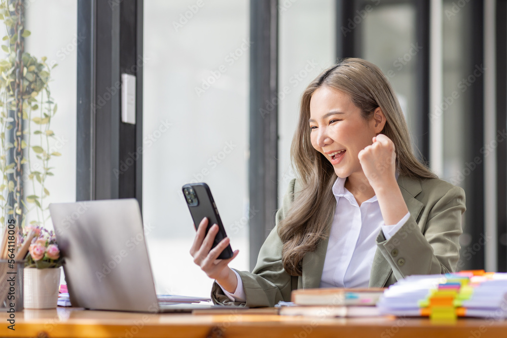 Everyday winner Excited Asian woman raising her arms while sitting at the desk in office, Happy excited employees work or business successful concept. Everyday winner Excited Asian woman raising her arms while sitting at the desk in office, Happy excited employees work or business successful concept.