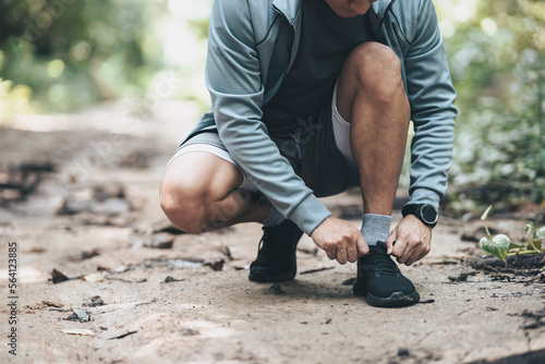Sport man tying jogging shoes in the forest. Outdoor workout, Healthy lifestyle concept.