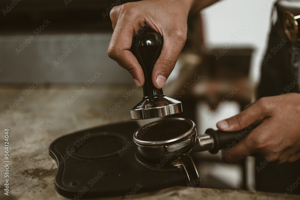 Barista using a tamper to press ground coffee into a portafilter. Coffee maker concept.. Barista using a tamper to press ground coffee into a portafilter. Coffee maker concept..