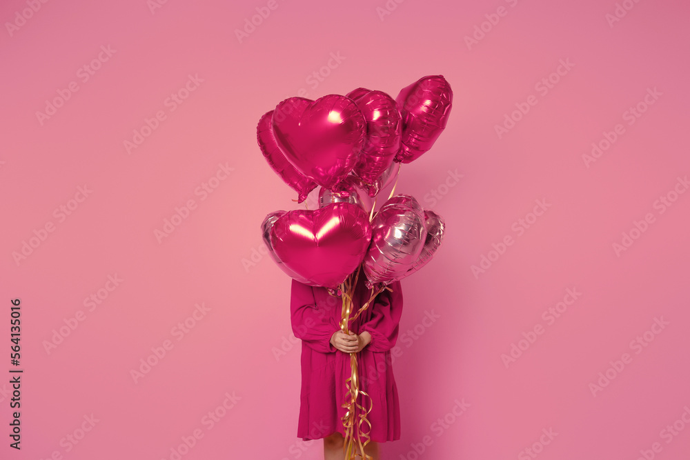Fototapeta premium A girl holds pink balloons in front of her on a pink background in a pink dress. Young woman on birthday holiday party. Valentine's Day, February 14.