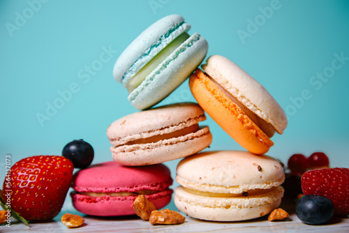 Colorful macarons. Small French cakes. Sweet and colorful french macaroons. Many tasty macarons with fresh berries, raspberries and blueberries, nuts and strawberries on a green background © MoreThanProd
