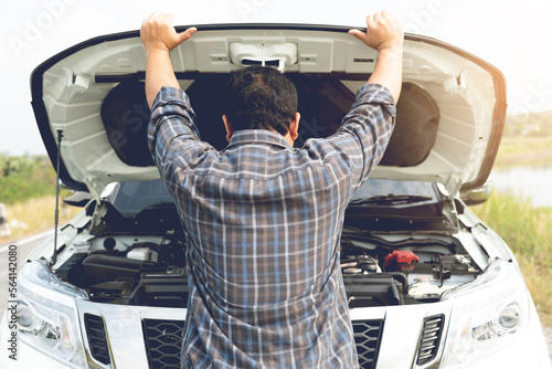 A young man having trouble with his broken car looks frustrated at the engine failure. photo