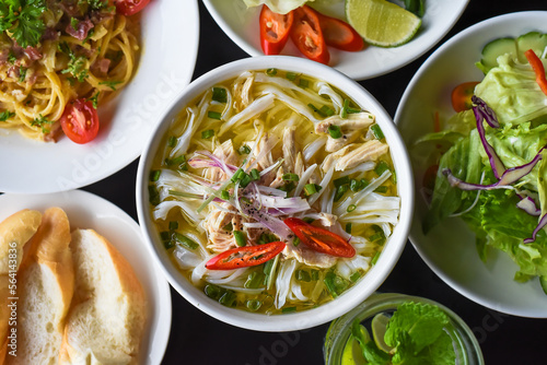 Chicken soup Pho ga in vietnamese style on black background with banh mi bread, salad and pasta carbonara