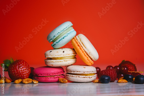 Colorful macarons. Small French cakes. Sweet and colorful french macaroons. Many tasty macarons with fresh berries, raspberries and blueberries, nuts and strawberries on a red background.