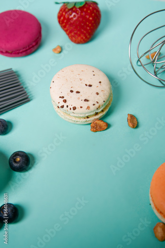 Colorful macarons. Small French cakes. Cooking, whisk, broken macarons, fruits, strawberries, raspberries and blackberries. Cooking process on a blue background, whisk, strawberries photo