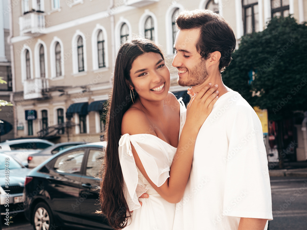Fototapeta premium Smiling beautiful woman and her handsome boyfriend. Happy cheerful family. Sexy couple posing in the street at sunrise. During romantic date at sunny summer day outdoors. Looking at each other