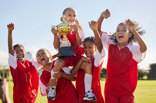 Football, team and trophy with children in celebration together as a girl winner group for a sports competition. Soccer, teamwork and award with sport player kids celebrating success outdoor