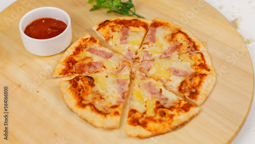 Closeup top view studio shot of tasty delicious Italian homemade mozzarella cheesy ham pineapple original Hawaiian pizza soft bread crust on wodden plate served on table with ketchup in restaurant