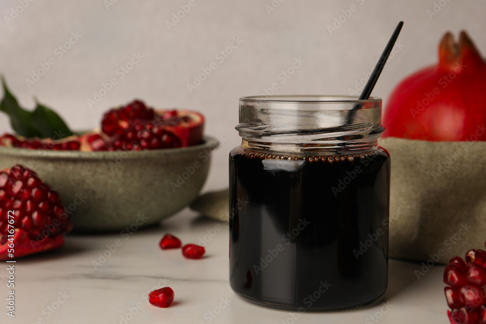Glass jar of tasty pomegranate sauce on white marble table. Space for text