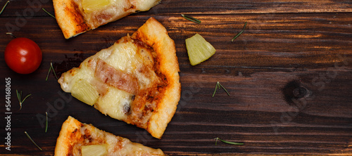 Closeup top view studio shot four pieces of hot oven baked tasty delicious Italian homemade ham and pineapple traditional Hawaiian soft bread crust pizza decorated on wooden table with tomatoes herbs