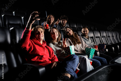 Friends take selfies before the start of the movie show. Smiling people look at the camera. Comfortable leather seats