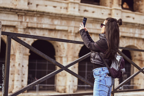 Rome Italy, travel tourism travel concept. Young beautiful woman taking a pictures of Colosseum and tourist crowds.