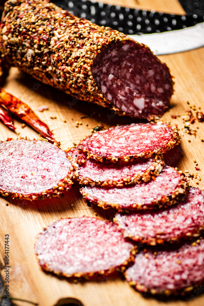 Pieces of salami sausage on a cutting board with pods of dried chili peppers. Pieces of salami sausage on a cutting board with pods of dried chili peppers.