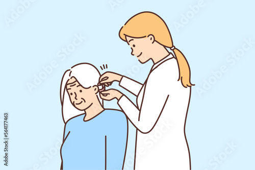 Female doctor install hearing aid to old patient 