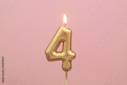 Gold birthday candle shaped as number 4 on pink background. photo