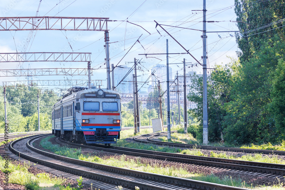 An old electric train on the railway tracks enters the city on a summer sunny day. An old electric train on the railway tracks enters the city on a summer sunny day.