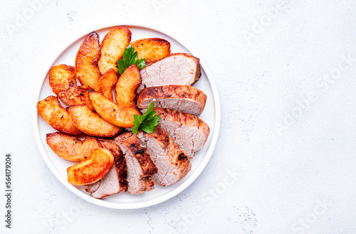 Baked pork tenderloin with quince or apple slices served on plate. White table background, top view photo