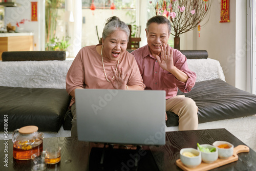 Senior couple waving with hands when video calling friends or family memebers photo