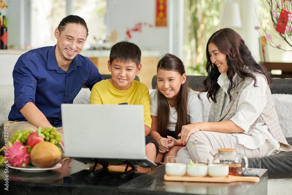 Smiling parents and children sitting in front of laptop, having tea with treats and video calling grandparents Smiling parents and children sitting in front of laptop, having tea with treats and video calling grandparents