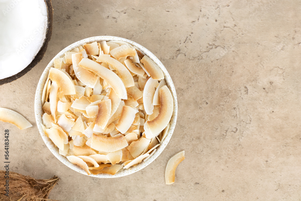 Coconut chips or coconut flakes in a white bowl and fresh coconuts on a