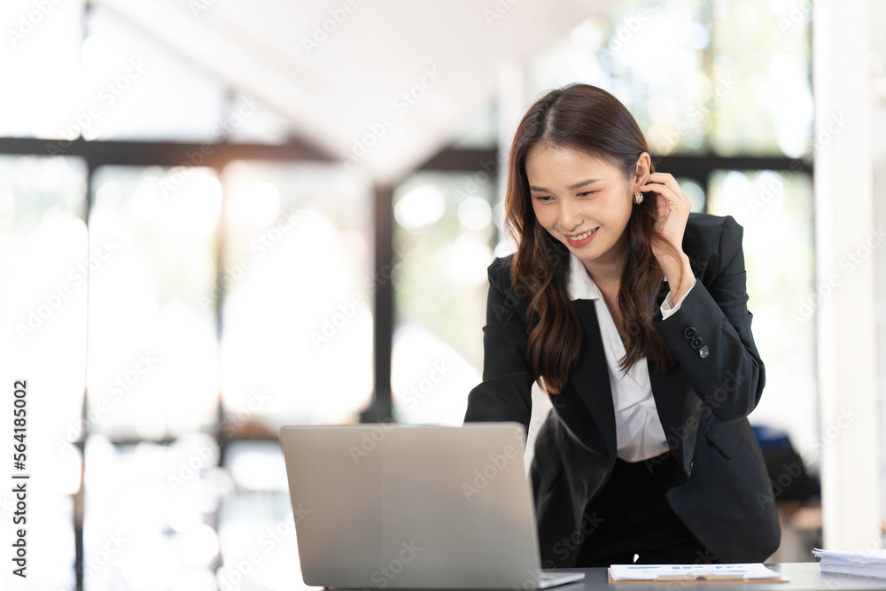 Focused young businesswoman standing at table in office, using laptop, looking at computer screen, reading or writing business email, searching information in internet, working on project Focused young businesswoman standing at table in office, using laptop, looking at computer screen, reading or writing business email, searching information in internet, working on project