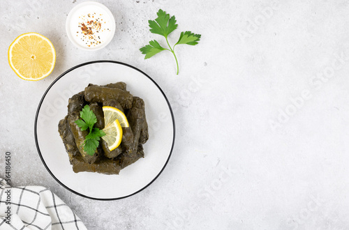 Dolma or tolma, sour cream, lemon, parsley on a gray background. Top view, copy space. Traditional Caucasian, Turkish, Armenian and Greek cuisine