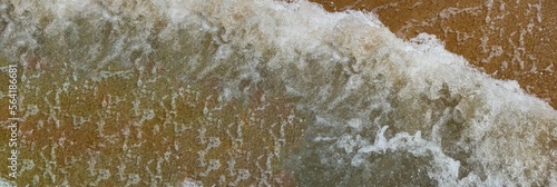 Panorama. Sea coast, top view close-up. Sea wave rolls on the sandy shore. Abstract pattern of sea foam and transparent water. World Ocean. Tour tourism. Tropical beach. Background with space for text