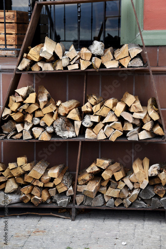 Chopped firewood stacked against the wall of the house for heating in the winter. A woodpile with a blank and stacked firewood from chopped dry wood for kindling and heating the house.