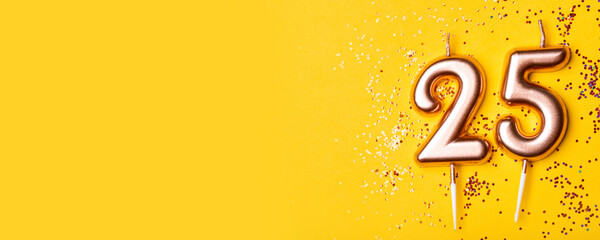 Gold candles in the form of number twenty five on yellow background with confetti. 25 years anniversary celebration.