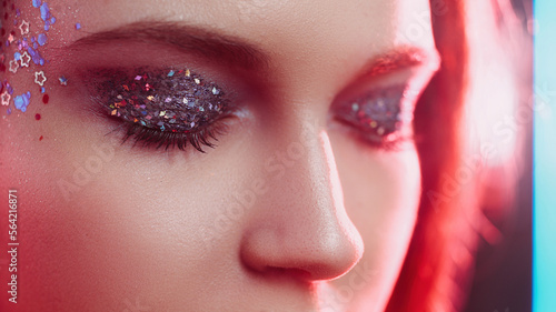 Glitter makeup. Neon light face. Disco look. Closeup of woman with closed eyes sparkling metallic eyeshadow artistic visage in red color glow.