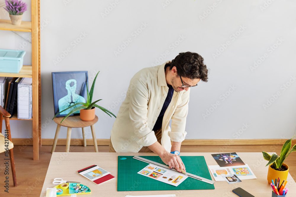 Male artist cutting pictures at table in creative studio Male artist cutting pictures at table in creative studio