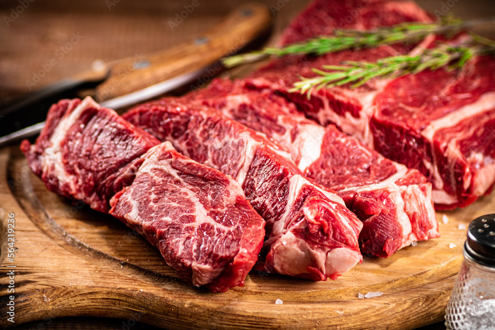 Raw beef on a cutting board with rosemary and spices. Raw beef on a cutting board with rosemary and spices.